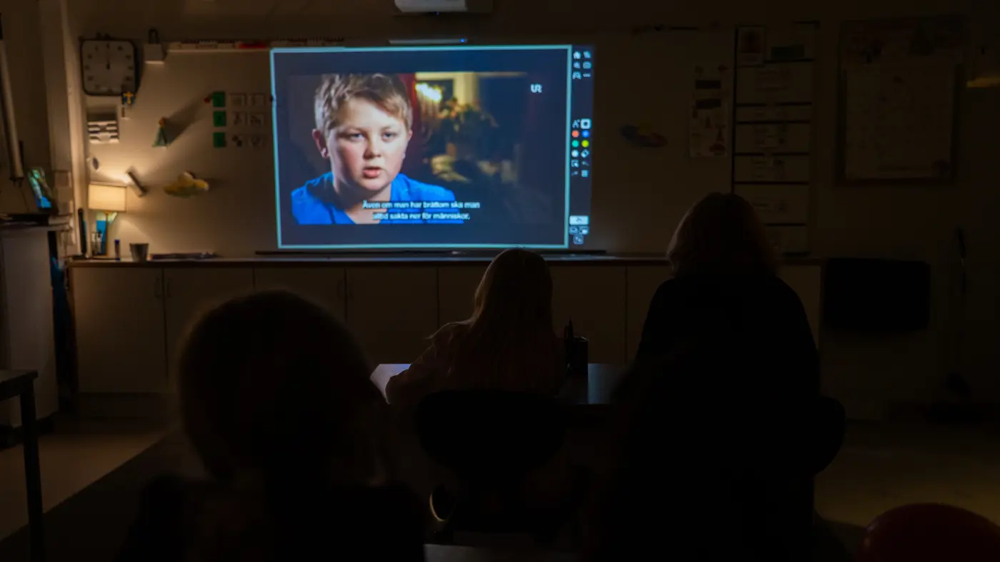 En grupp skolbarn sitter i ett mörkt klassrum och tittar på en film.
