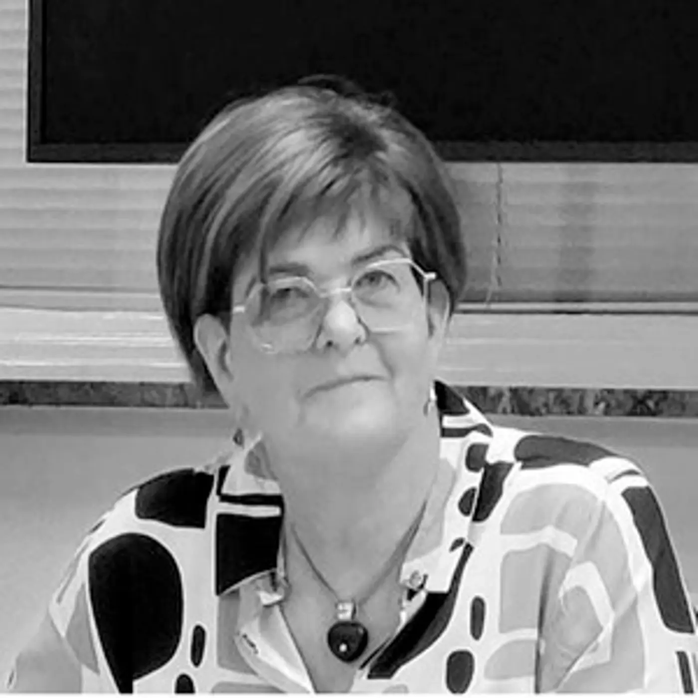 Svartvit porträttbild på en kvinna med kort hår, glasögon och mönstrad blus.