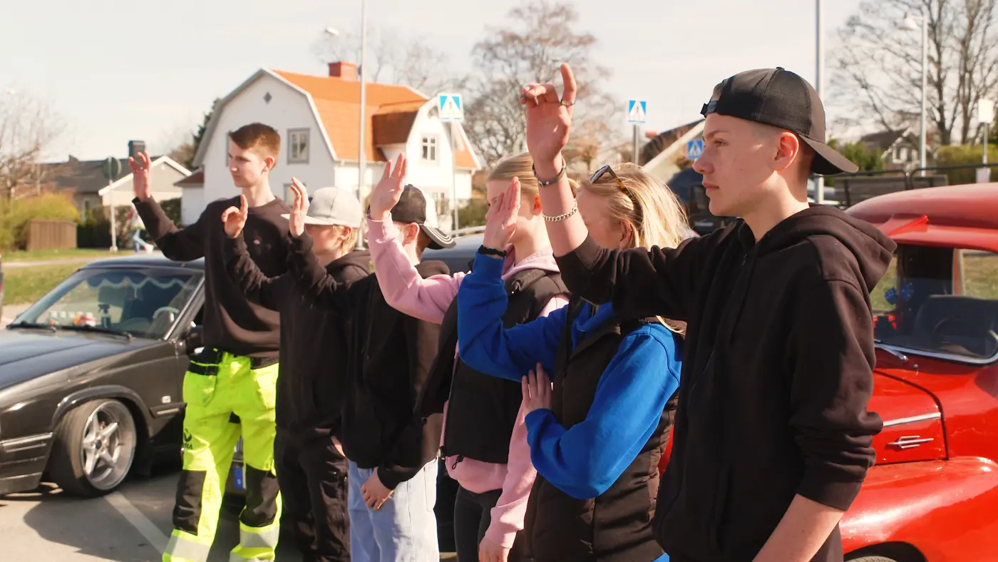 Sex ungdomar står framför några A-traktorer och räcker upp handen.