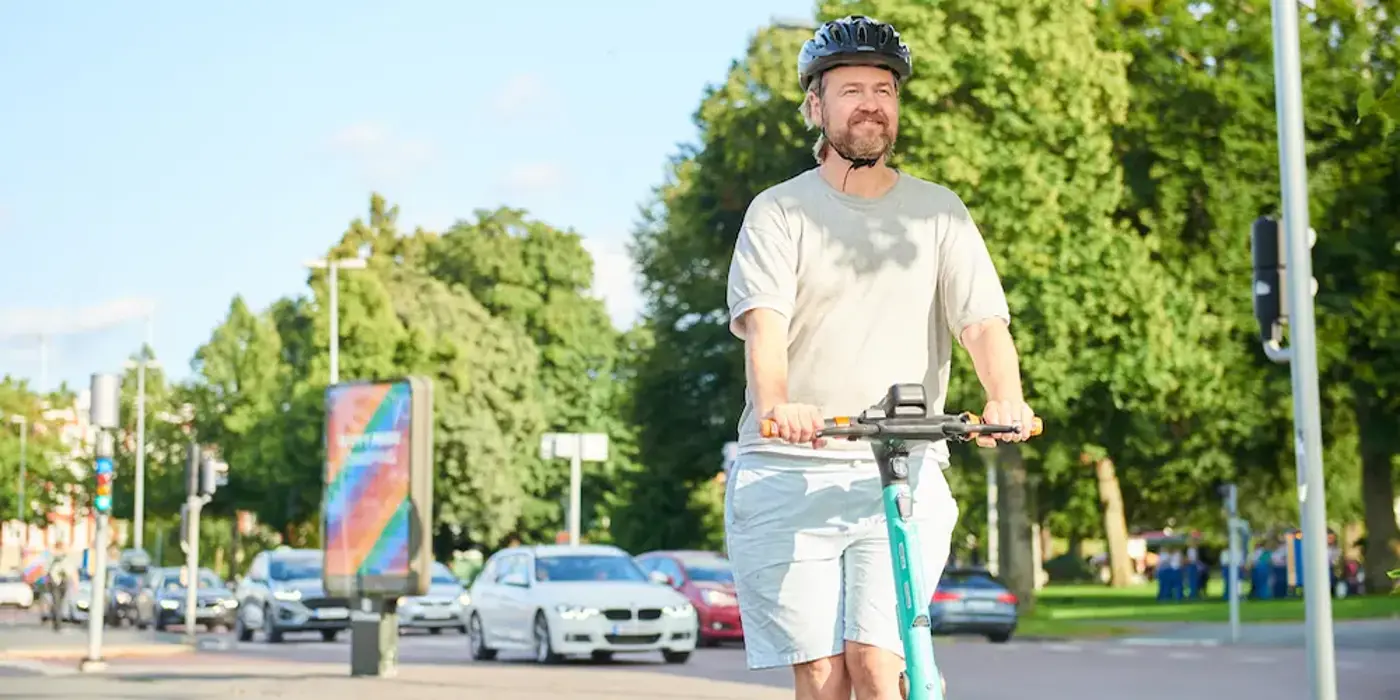 En person med hjälm på huvudet kör en elsparkcykel i stadsmiljö.