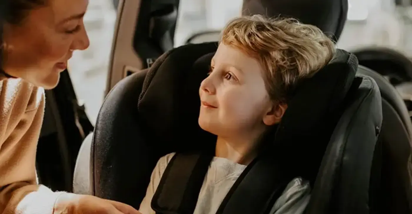 Ett barn sitter i en bakåtvänd bilbarnstol och en förälder lutar sig fram mot barnet.