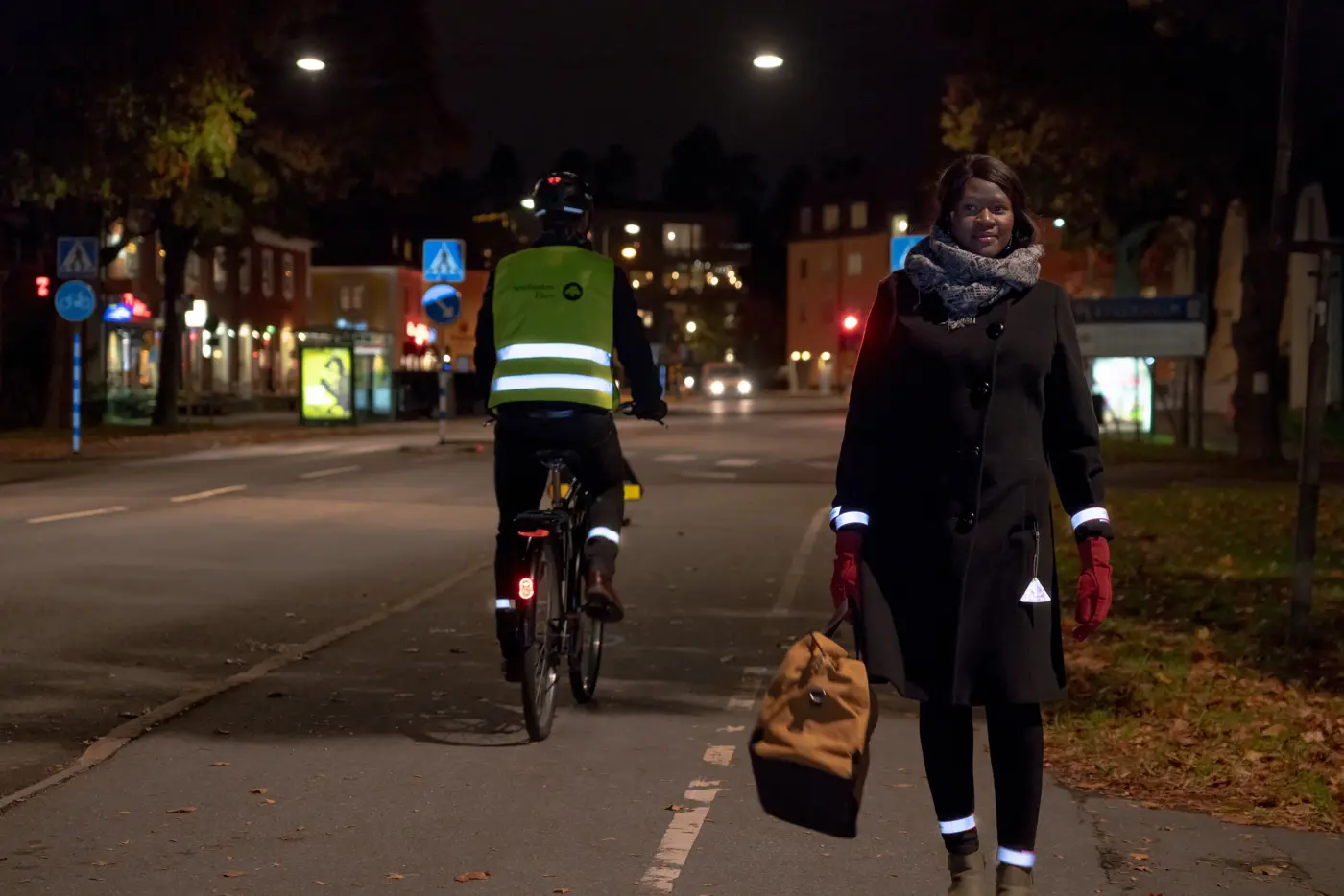 En kvinna med mörka kläder och reflexer på armar, ben och fickor promenerar i mörker.