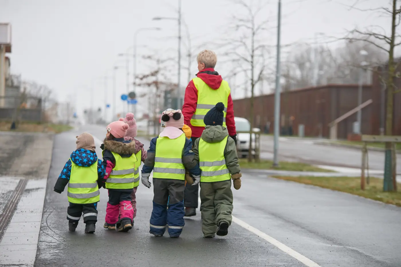 En förskolegrupp med reflexvästar promenerar på en gångväg.