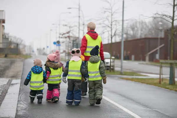 En förskolegrupp med reflexvästar promenerar på en gångväg.