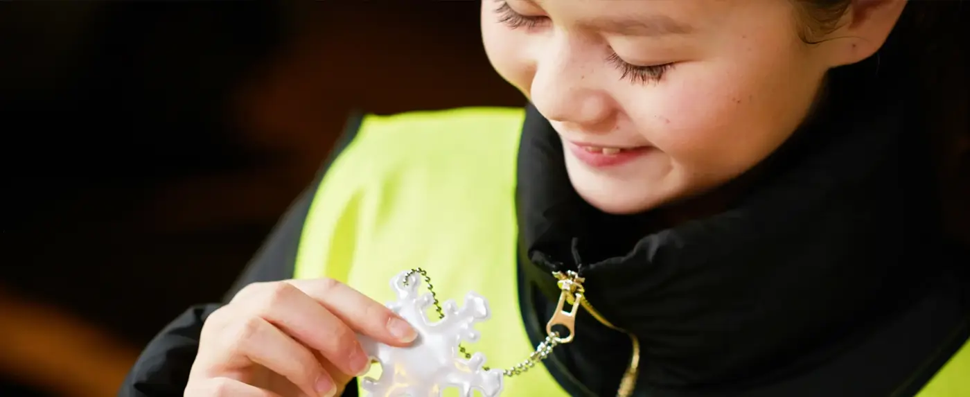 Ett barn håller i en reflex som är fastsatt i dragkedjan på jackan, barnet bär även reflexväst.