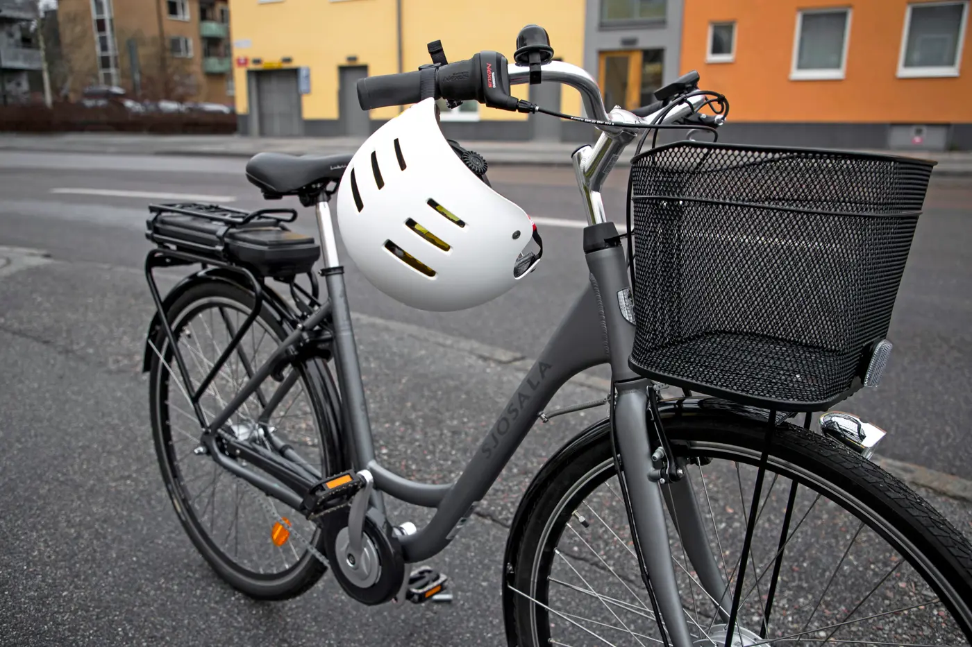 En elcykel står uppställd på gatan och på styret hänger en hjälm.