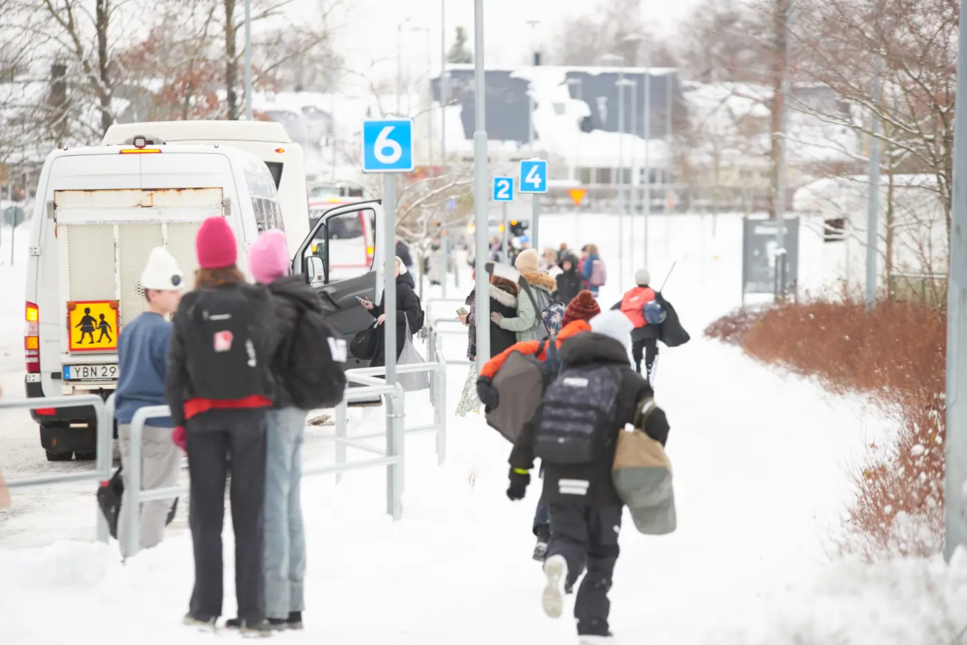 Bilar kör och barn promenerar utanför en skola i vintertid. Det är snö på marken.