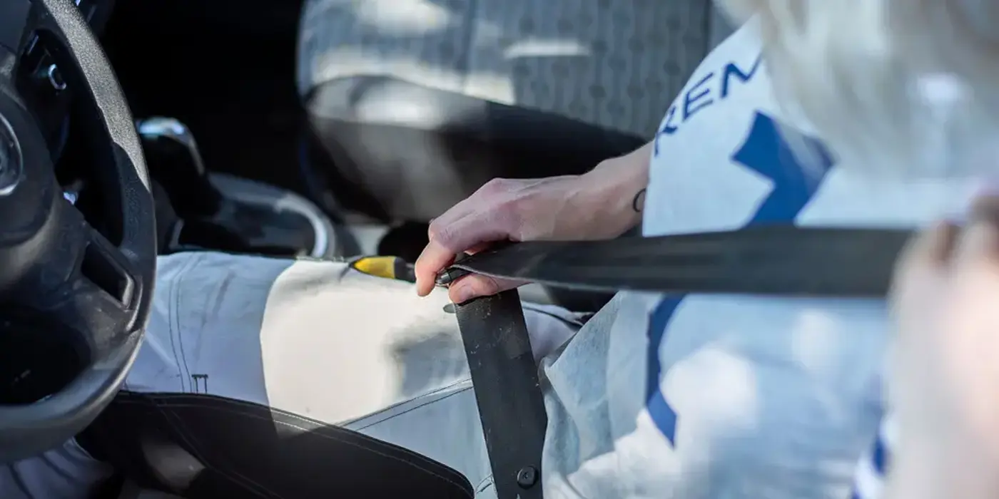 Person sitter i förarsätet på en bil och knäpper sitt bilbälte.