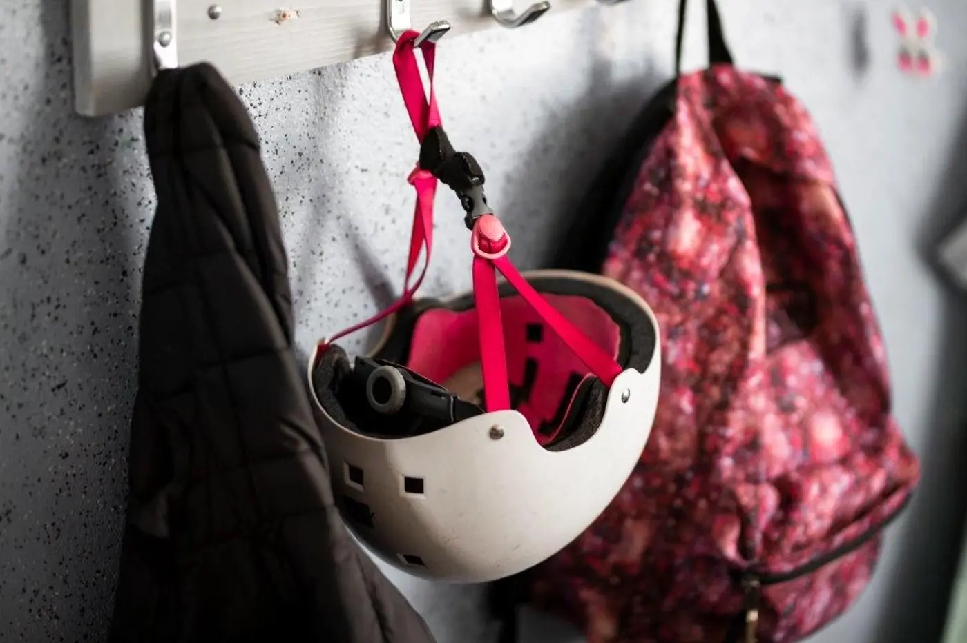 En vit cykelhjälm hänger på en krok jämte en ryggsäck och en jacka.