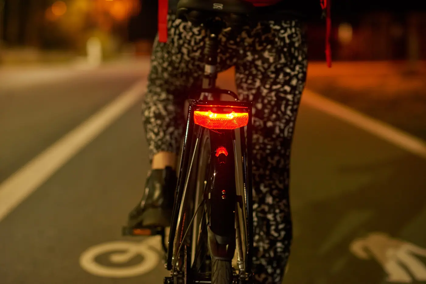 En person cyklar i mörker och baktill lyser en röd cykellampa.