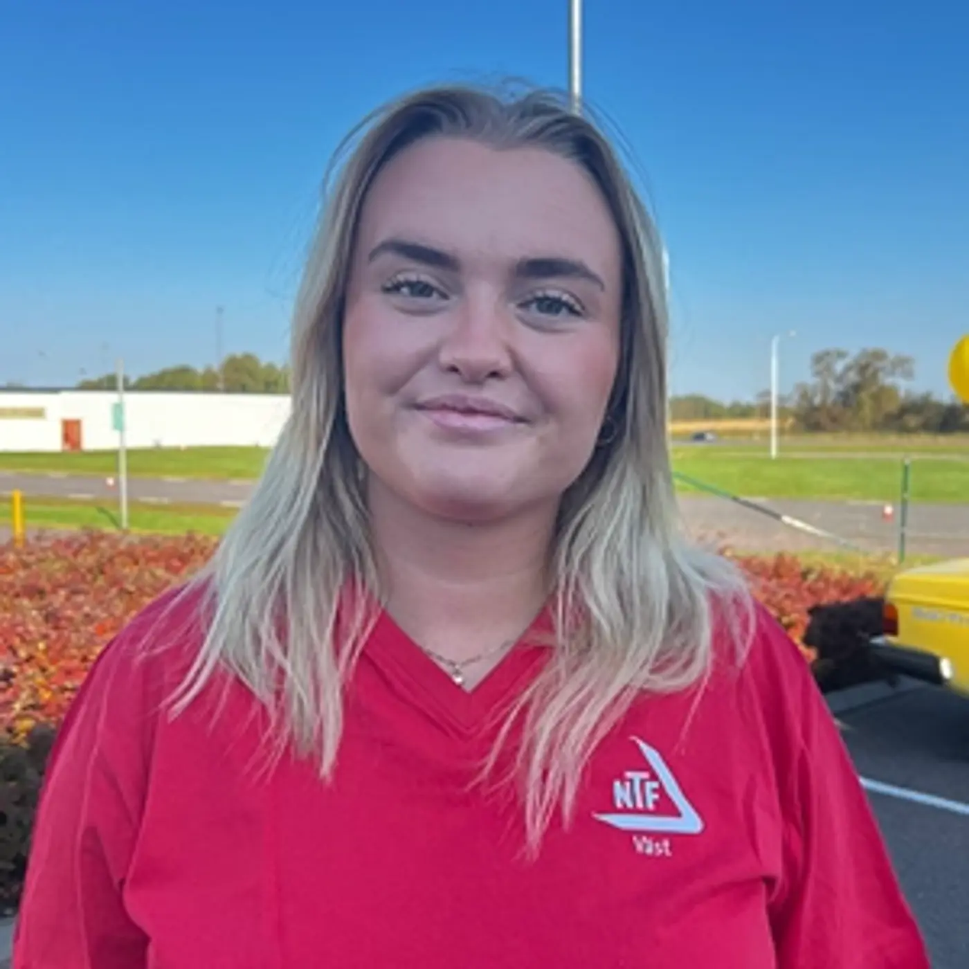 Porträttbild på en leende kvinna med blont hår och en röd t-shirt.