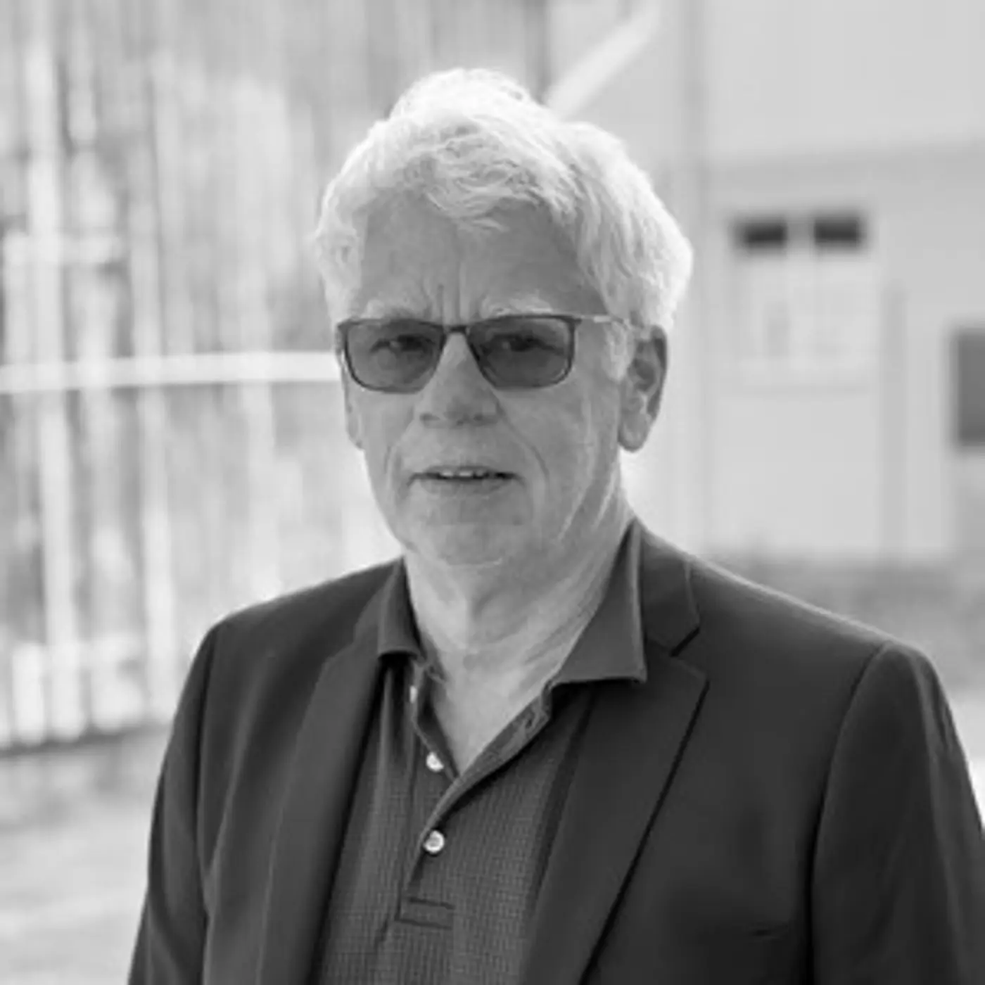 Svartvit porträttbild på en äldre man med glasögon och kavaj.