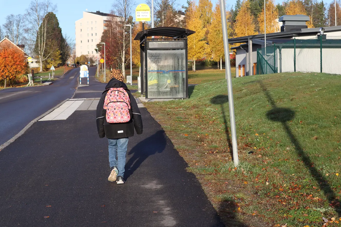 Ett skolbarn med ryggsäck mot en busshållplats.