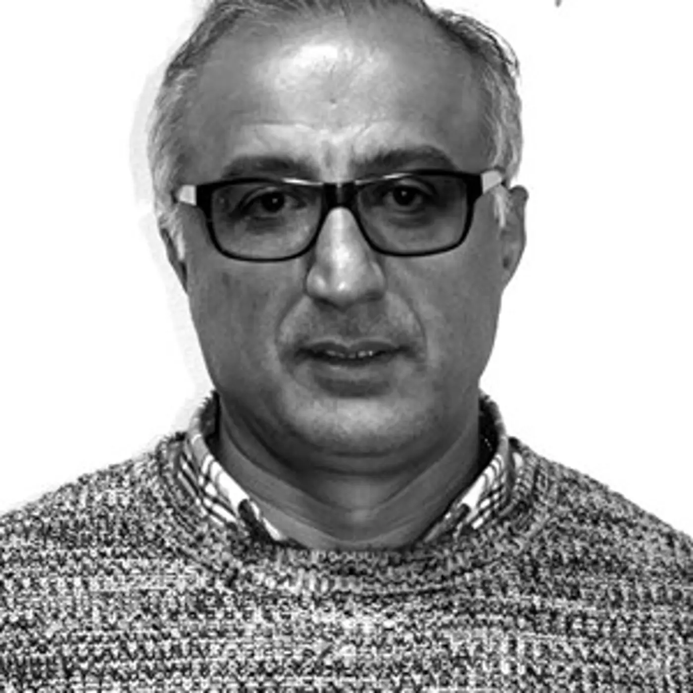 Svartvit porträttbild på en äldre man med glasögon och stickad tröja.