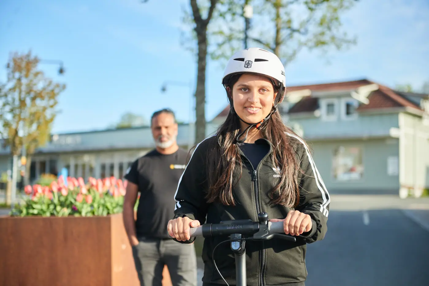 En pappa tittar på sin dotter som ska köra iväg på en elsparkcykel.