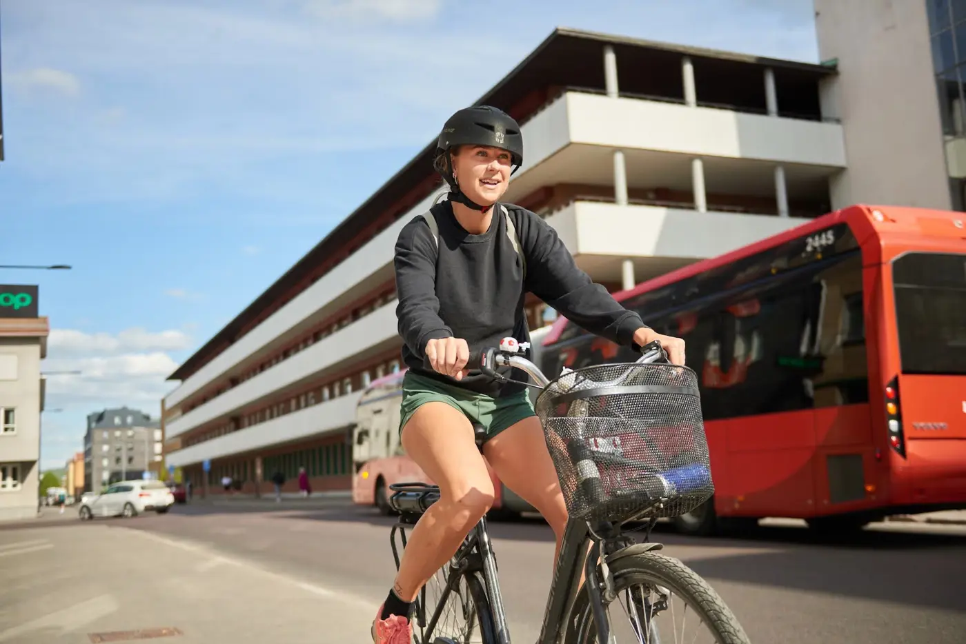 En ung vuxen med cykelhjälm på huvudet kommer cyklandes i stadsmiljö