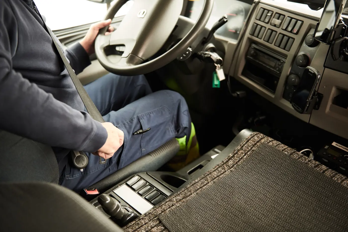 En lastbilschaufför sitter framför ratten och spänner fast säkerhetsbältet.