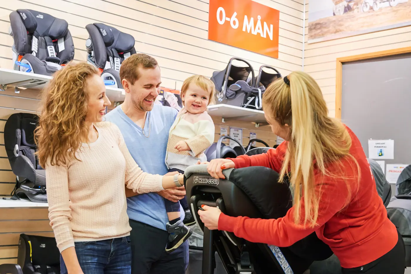 En familj står i en butik med bilbarnstolar och får rådgivning av ett butiksbiträde.