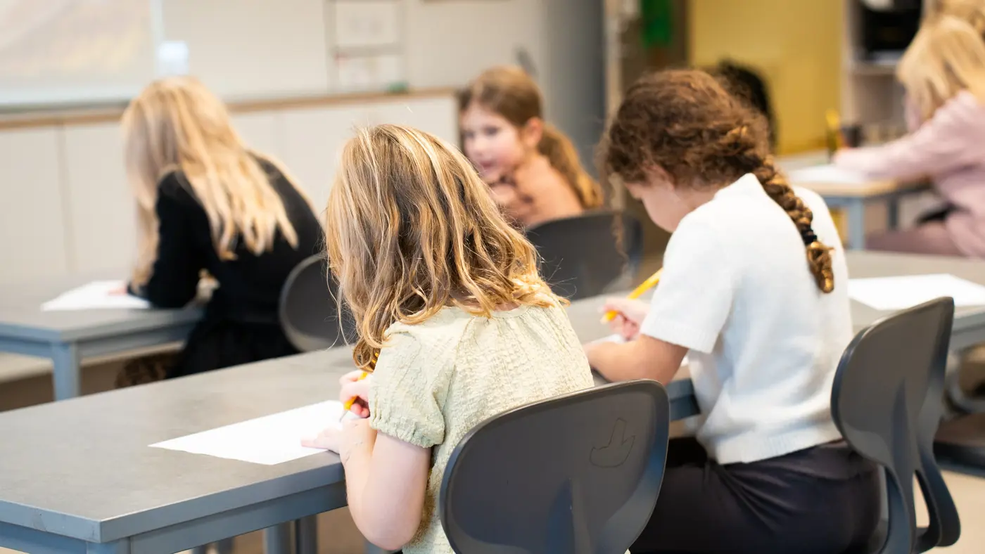 En grupp skolbarn sitter i sina bänkar och skriver.
